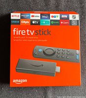 Front of sealed orange box showing Fire TV Stick with Alexa Voice Remote and logos of popular streaming apps.