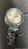 Front view of black spotlight showing the reflective lens and bulb inside with coiled attached power cord.