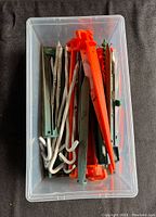 Top-down photo of a plastic container filled with various tent pegs in metal and plastic, different shapes and sizes.
