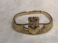 Front view of 14kt gold Claddagh ring showing crowned heart held by two hands.