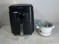 Ultrean AF03 black air fryer next to white Sunbeam small crock pot with floral design and glass lid