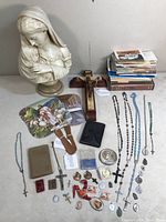 Wide view of all items in the lot including the ivory-colored Virgin Mary bust, various rosaries, crucifixes, prayer books, religious medals, and pamphlets.
