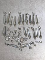 Multiple hanging lamp crystals laid out on a flat surface, showing long prism shaped crystals and smaller round faceted crystals, some with small attached broken pieces.