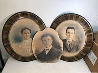 Three large vintage oval photos, two in oval brown period frames, one unframed with visible damage, arranged together.