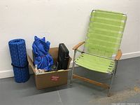 Photo showing green webbed camping chair, blue rolled sleeping mat, and cardboard box with various camping items