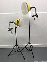 Full view of two yellow photographic lamps on black adjustable tripod stands against a white wall.