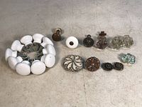 Full view of all knobs and pulls arranged on floor, showing variety of porcelain, metal, and glass items.