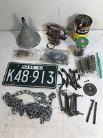 Full view of various random metal and hardware salvage items including license plate, chain, hooks, brackets, funnel, and jars with parts