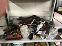 Shelf containing a mix of various small vintage items including a dark brown Breyer horse figurine lying on its side, metal dishes, toy cars, sunglasses, flags, and collectible patches.