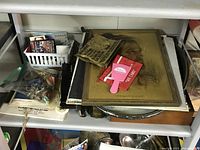 Close-up of ephemera cards, small parts in a plastic basket, vintage tools, and handheld decorative items on shelf