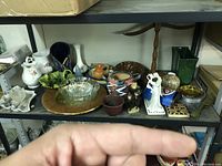 Shelf showing a variety of pottery, glass, and collectible items with packaging boxes on top shelf