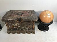 Front view of the wooden chest showing carved and painted designs and the small globe on a stand next to it.