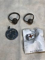 Two sterling silver rings, a round silver pendant with cutout heart design, and a London-themed sterling silver pendant on original packaging.