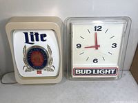 Photo of both items side by side: a Miller Lite lighted sign on the left and Bud Light clock on the right