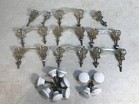 Overview of vintage glass and porcelain knobs and pulls spread on a grey surface, showing multiple glass fluted knobs, glass pulls, and white porcelain knobs.