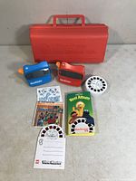 Two vintage View-Master viewers (blue and red), several View-Master reels including Fat Albert and Sesame Street sets, a slide folder, and illustrated reels albums displayed together.