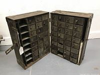 Front view of the open trunk showing two sections of multiple small metal drawers with leather tabs plus vertical open compartments on left section.