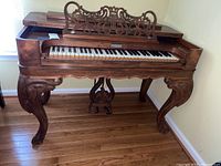Front view of Victorian rosewood melodeon with music rack folded down revealing 61-key keyboard and carved legs.