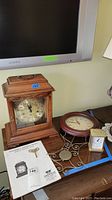 Photo of Emperor Bristol mantel clock on a table with winding key and assembly instructions, alongside Howard Miller clock and Chaney pendulum clock.