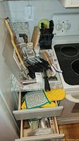 Overview of knives, cutting boards, utensils, pot holders in kitchen drawer and on counter.