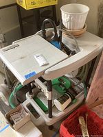 Overview of backyard cart with hose, faucet components, and accessories on bottom shelf, plus two unopened boxes of HydroWash on the ground near the cart.