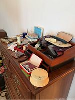 Overview showing wooden jewelry box with compartments, eyeglasses cases, mirrored tray, and assorted small items and jewelry on top of a wooden dresser.