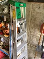 Full view of the 6ft aluminum ladder showing steps, green top, and locking supports in a garage environment.