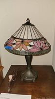 Full view of Tiffany style stained glass lamp with floral pattern shade and metal base, with power cord visible.