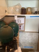 Three green Advent outdoor speakers on a shelf with bubble wrap and River Cottage Garden outdoor lamp covers in varying colors (amber, brown, green), with wires visible.