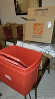 Red plastic storage bins with lids in front with medium Home Depot box behind