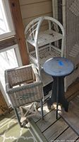 Full view of the two wicker plant stands together on a covered porch with visible wear and paint chipping.