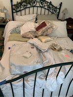 Queen bed with assorted pillows, blankets, packaged mattress pad, and comforter displayed on bed with metal frame