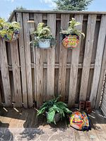 Three colorful ceramic wall pocket planters with faux plants, colorful floral designs, shown hanging on wooden fence and one on the ground along with a broken ceramic planter piece.