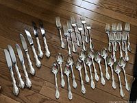 All flatware pieces laid out on hardwood floor showing forks, spoons and knives
