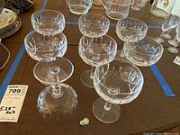 Top-down view of all eight etched Waterford champagne glasses arranged together showing crystal etching and one bottle with sticker.