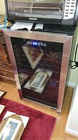 Front view of the wine cooler showing glass door, stainless steel trim, digital display illuminated.
