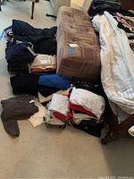 Overall view of assorted folded women's clothing including sweaters, tops, pants and some shorts arranged on carpet floor and sofa.