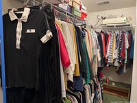 Shows black polo shirt with white collar and sleeve detail plus assorted women's clothing hanging on rack