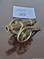 Angled side view of the brass miniature cannon showing wheels and barrel detail on a reflective surface.