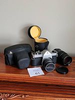 Asahi Pentax camera with original lens, extra 135mm lens, and both protective cases on wooden surface.