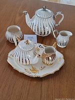 Full view of the vintage English Sadler porcelain tea set including teapots, creamers, sugar bowl, and serving plate with gold floral accents on wooden surface.