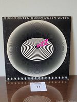 Front cover of 1978 Queen Jazz vinyl LP showing abstract circular black and white design with pink text.