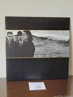 Front of U2 The Joshua Tree vinyl album gatefold cover showing band members in a desert scene under a black background with gold border.