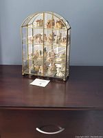 Front view of the brass framed glass display cabinet with 16 ceramic Wade figurines arranged on 4 shelves.