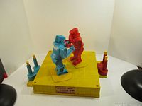 Wide shot showing red and blue robots on yellow boxing ring base with controllers