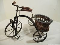 Front angle view of the metal bicycle planter showing wooden handle and seat, metal frame, and wicker basket.