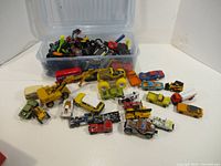 Box containing various toy cars, trucks, and construction vehicles spread out in front showing size and variety.