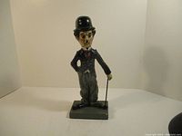 Front view showing full figure of the Charlie Chaplin statue with bowler hat, suit, bow tie, and cane on a rectangular base.