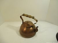 Copper kettle angled to show side and spout with wooden handle and lid.