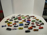 Wide angle photo showing approximately 40 die cast cars of various styles and colors arranged on white background
